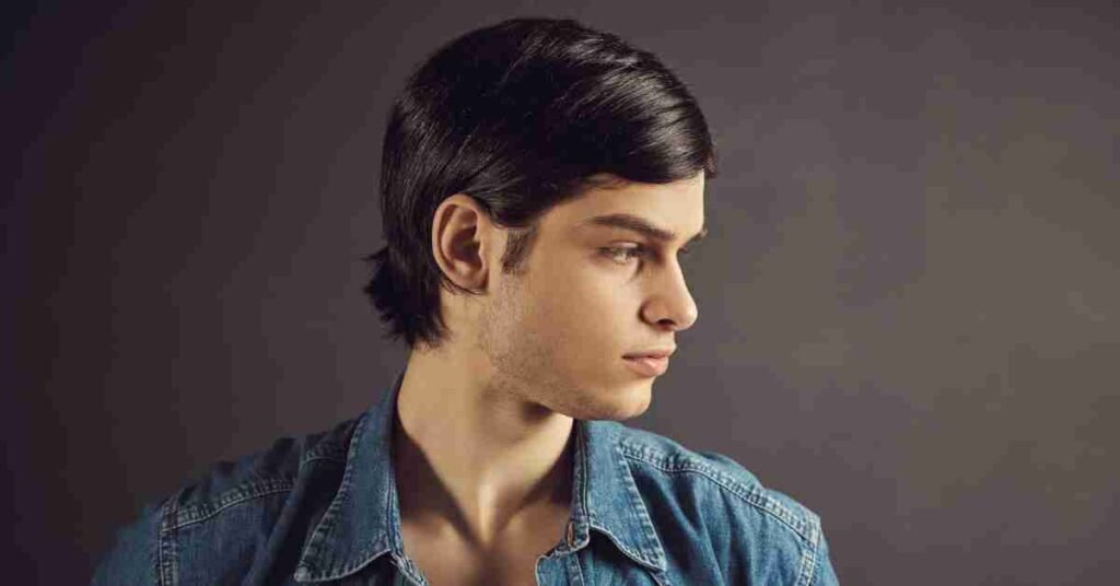 A young man profile showcasing a modern mullet haircut for boys, featuring sleek, side-parted hair on top that flows into a tapered length at the back